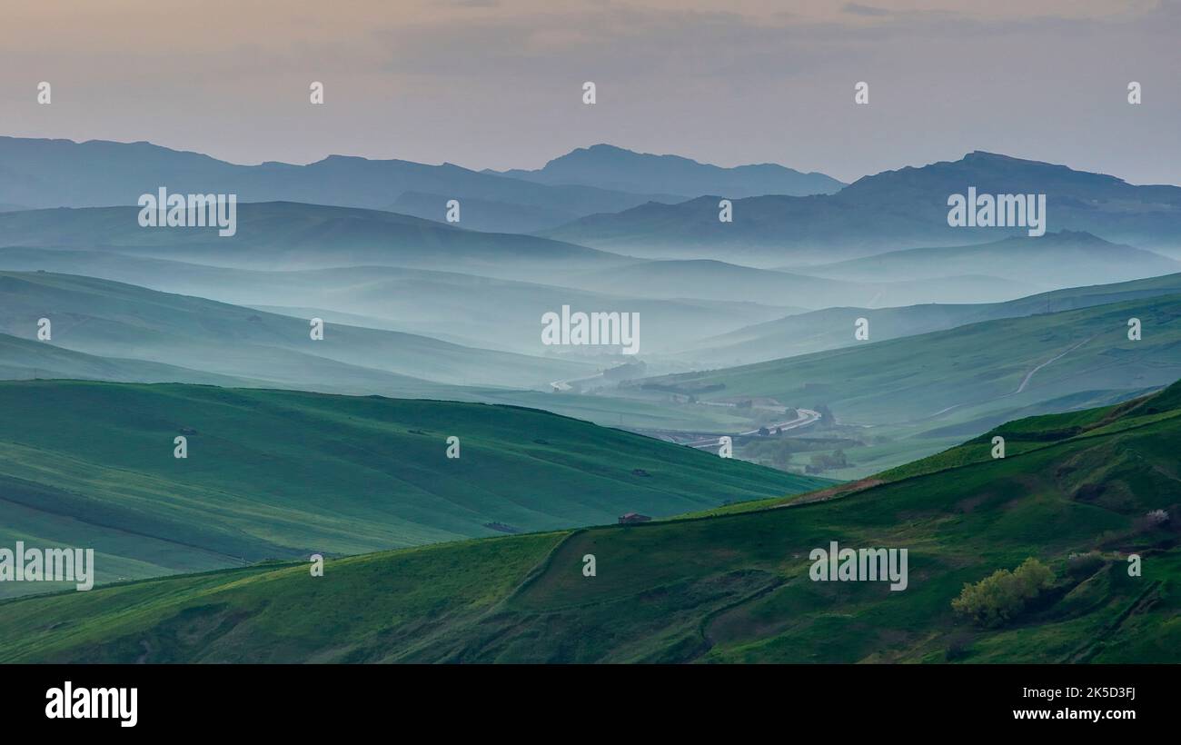 Italy, Sicily, Madonie National Park, spring, morning fog, back-to-back hill ranges, green fields, haze, single houses Stock Photo