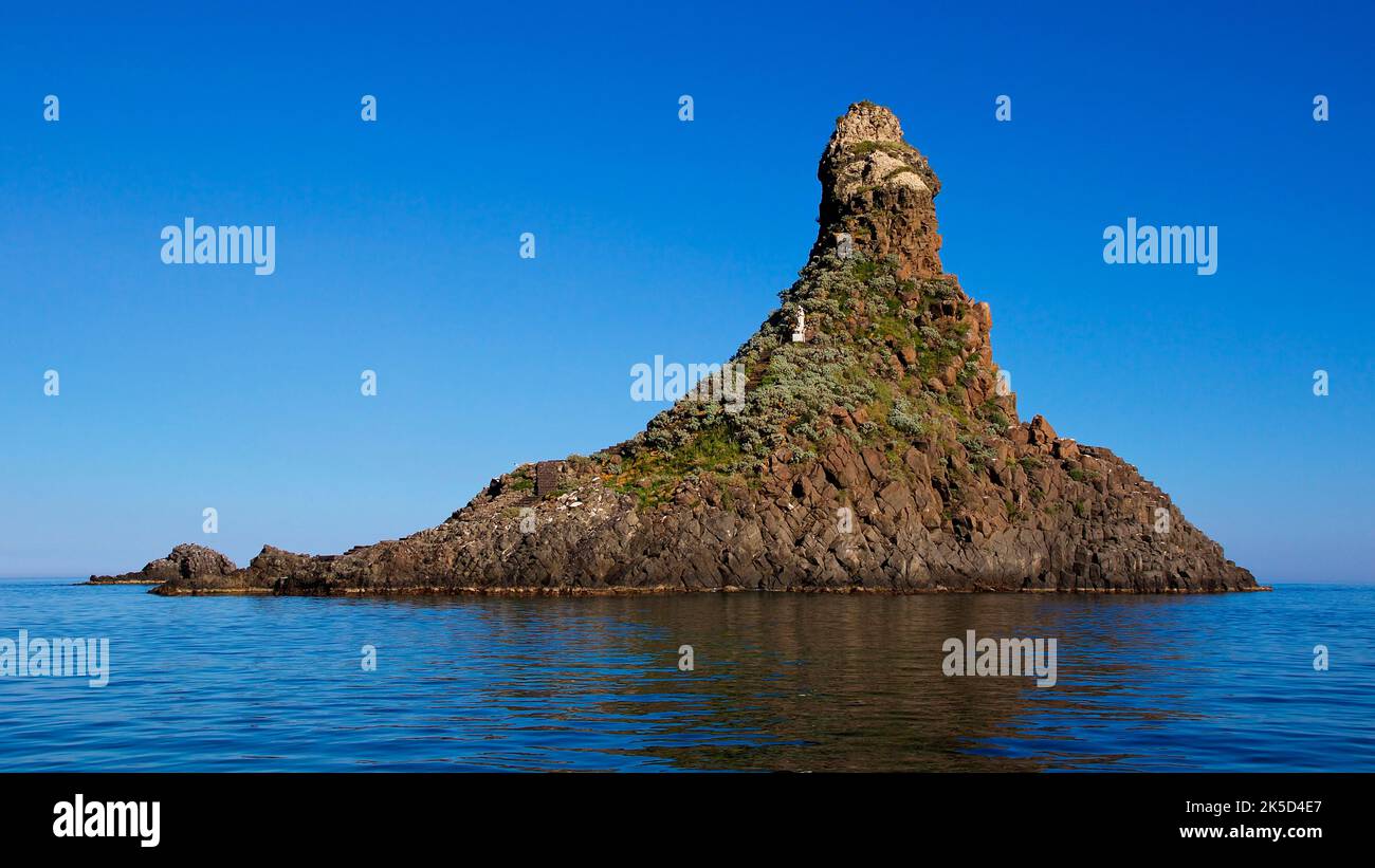 Italy, Sicily, Cyclops Coast, Cyclops Island, high rocky outcrop, forested small island, sea dark and calm, blue sky, cloudless Stock Photo