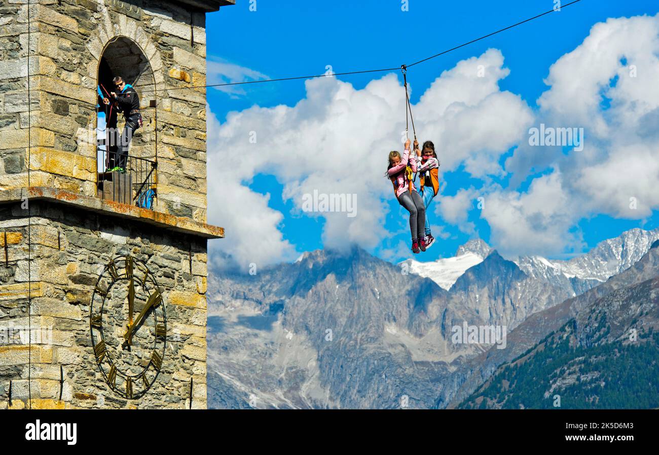 Two girls hang on the rope of a zipline and slide from the church tower to the ground, test of courage at the Chinderwältfäscht, children's world festival, Heidadorf Visperterminen, Valais, Switzerland Stock Photo