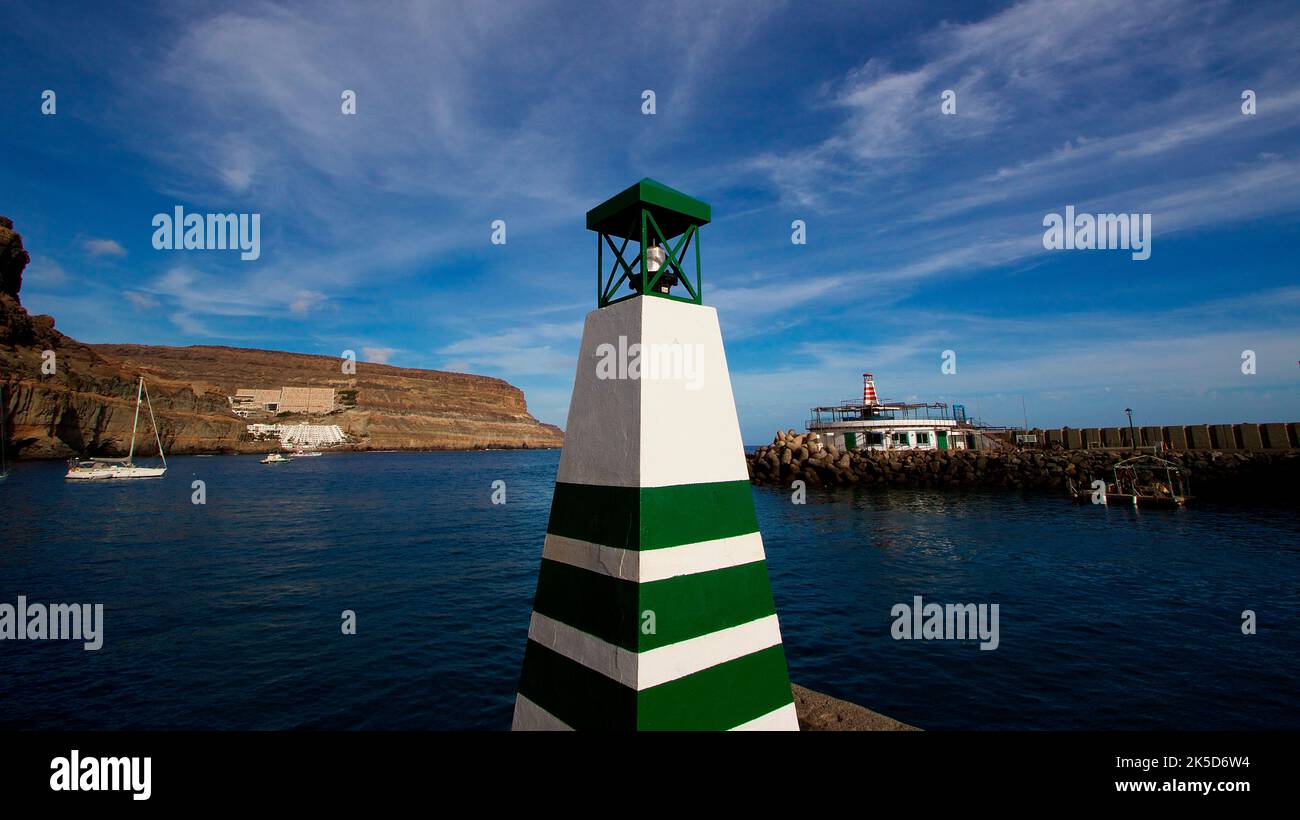Spain, Canary Islands, Gran Canaria, southwest coast, Puerto de Morgan, Little Venice, wide angle shot, green and white square beacon in foreground, boats in middle ground, rocky coast in background, dark blue sea, blue sky with white stripe clouds Stock Photo