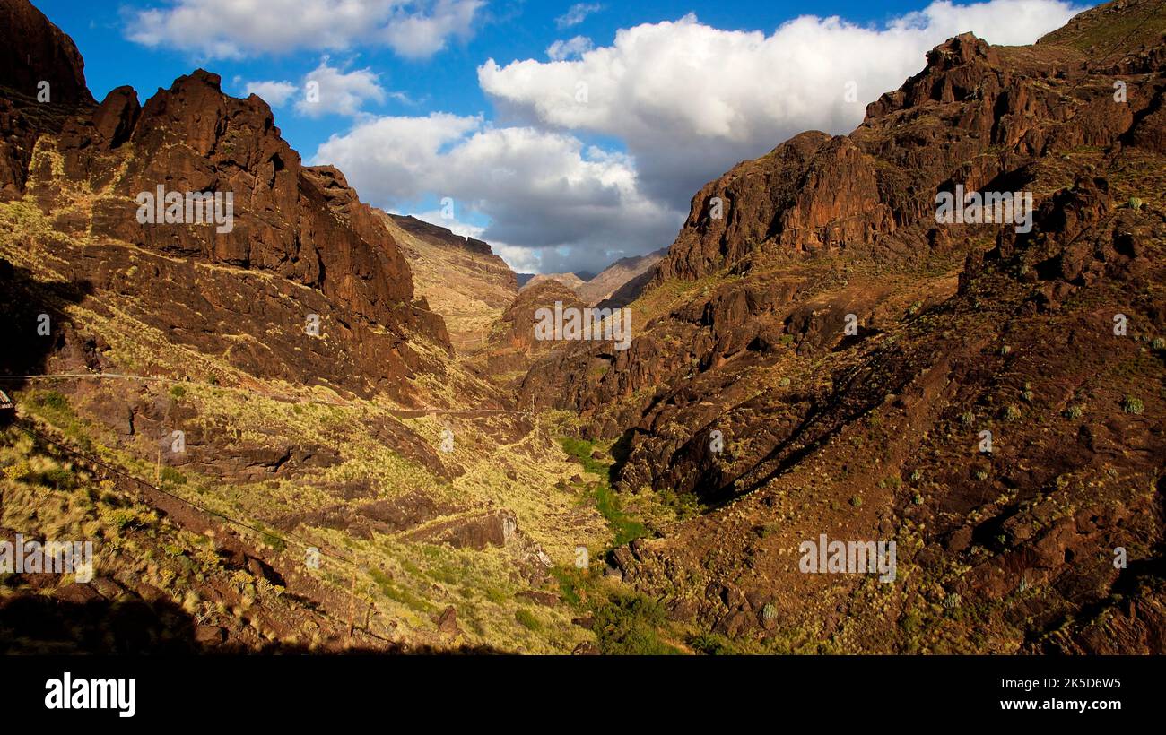 Spain, Canary Islands, Gran Canaria, Barranco de la Aldea, view into the barranco to the north, rock towers, steep slope, slopes overgrown with green, blue sky with cumulus clouds Stock Photo