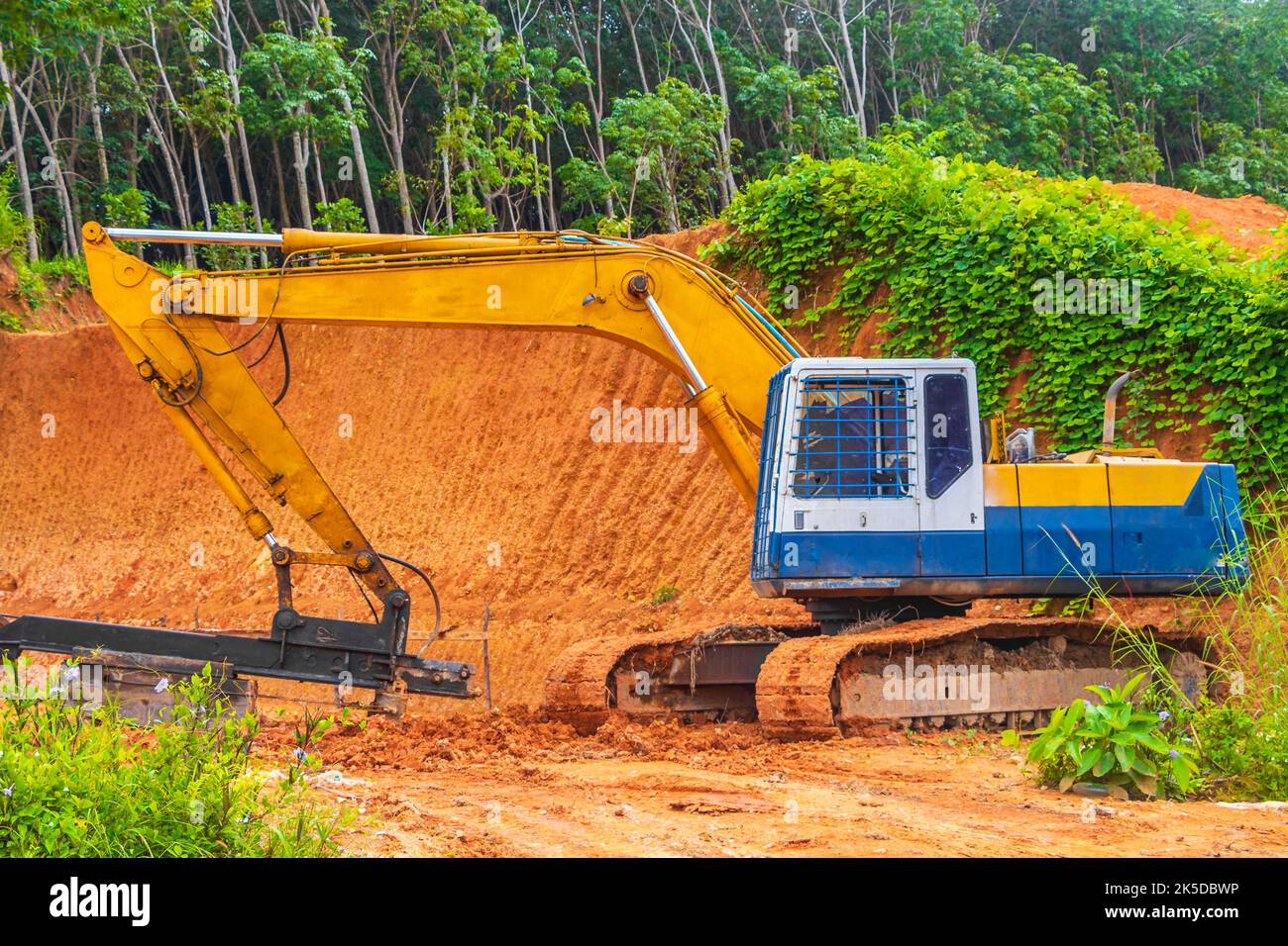 Big yellow excavator digs destroys forest jungle in Sakhu Thalang on Phuket island Thailand in Southeastasia Asia. Stock Photo