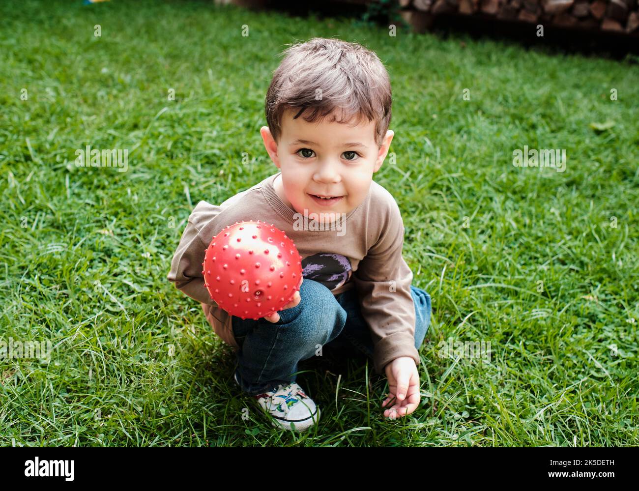 super cute young boy is Playing with a ball on the grass in the backyard Stock Photo