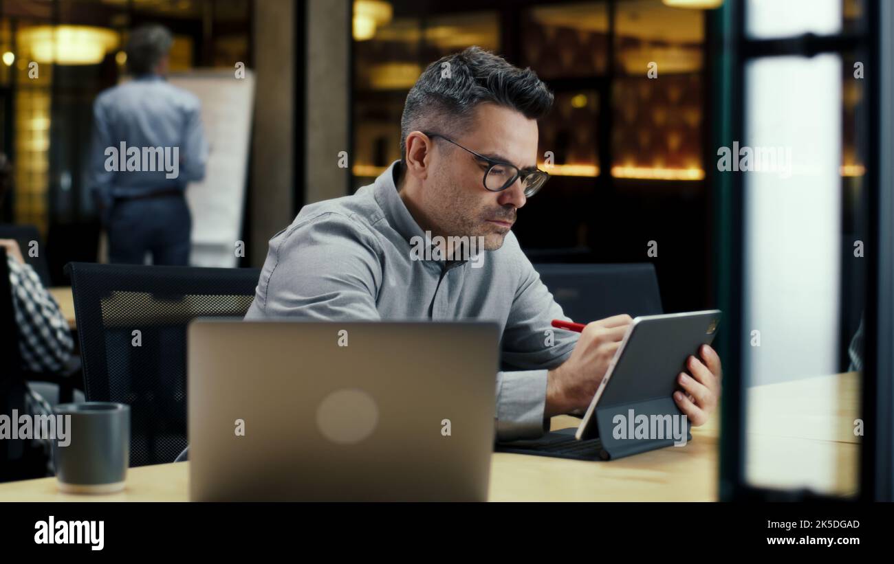 Male office worker, using tablet computer and digital pencil, working in modern office on startup project, business strategy or design of website. Work in IT company Stock Photo