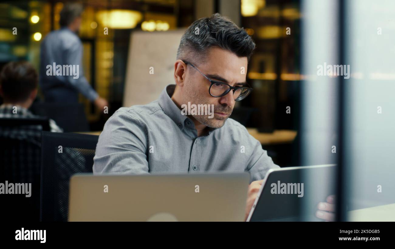 Male office worker, using tablet computer and digital pencil, working in modern office on startup project, business strategy or design of website. Work in IT company Stock Photo