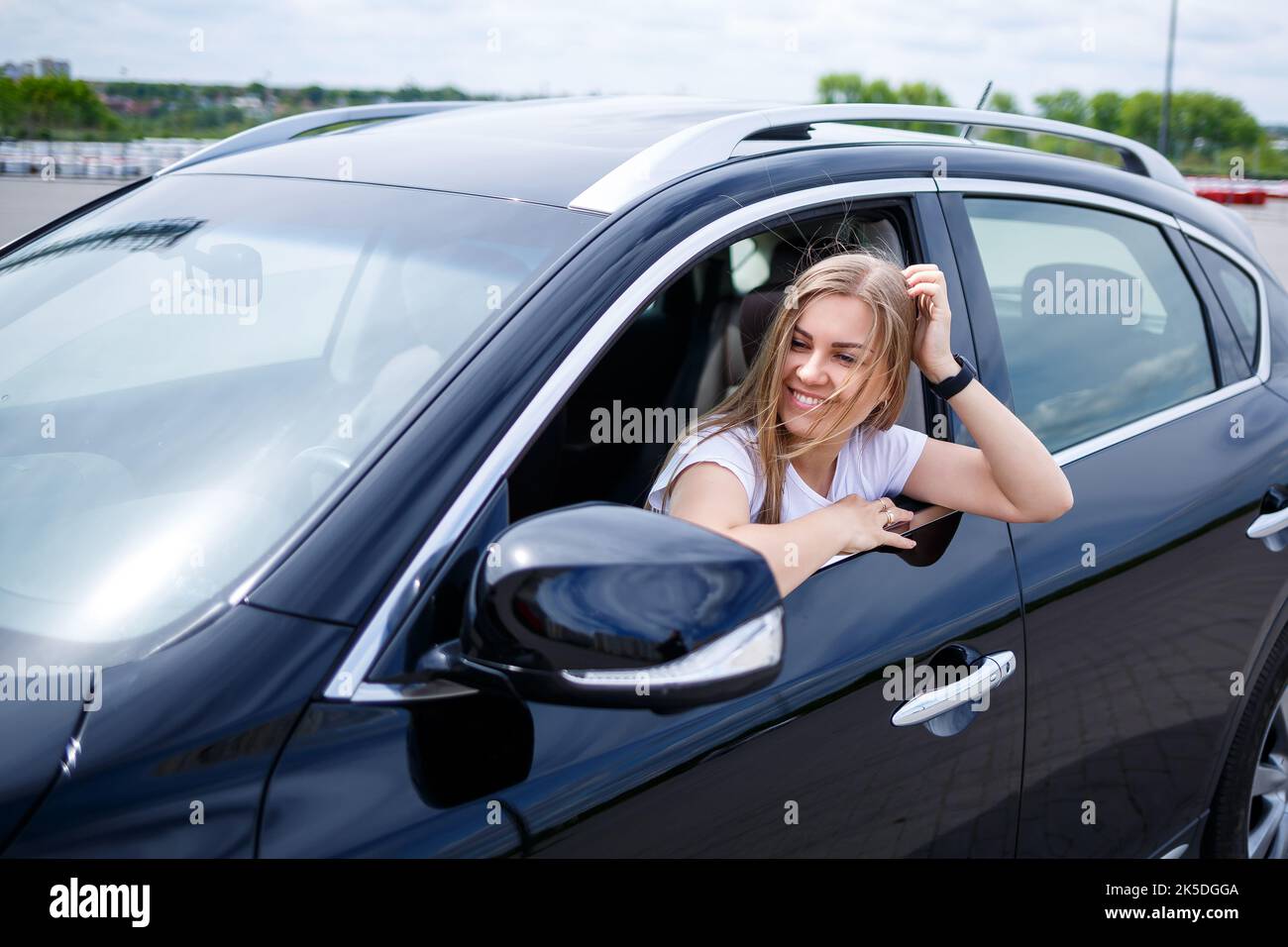Young beautiful woman with long hair sits in a black car at a parking
