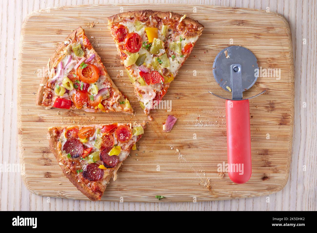 Pizza with salami, pepperoni peppers, tomatoes and onions on a table and a pizza cutter next to -  view from above Stock Photo