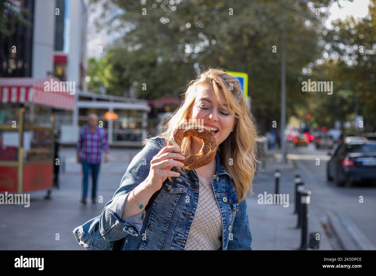 Blonde woman eating traditional Turkish bread bagel on the street. Stock Photo