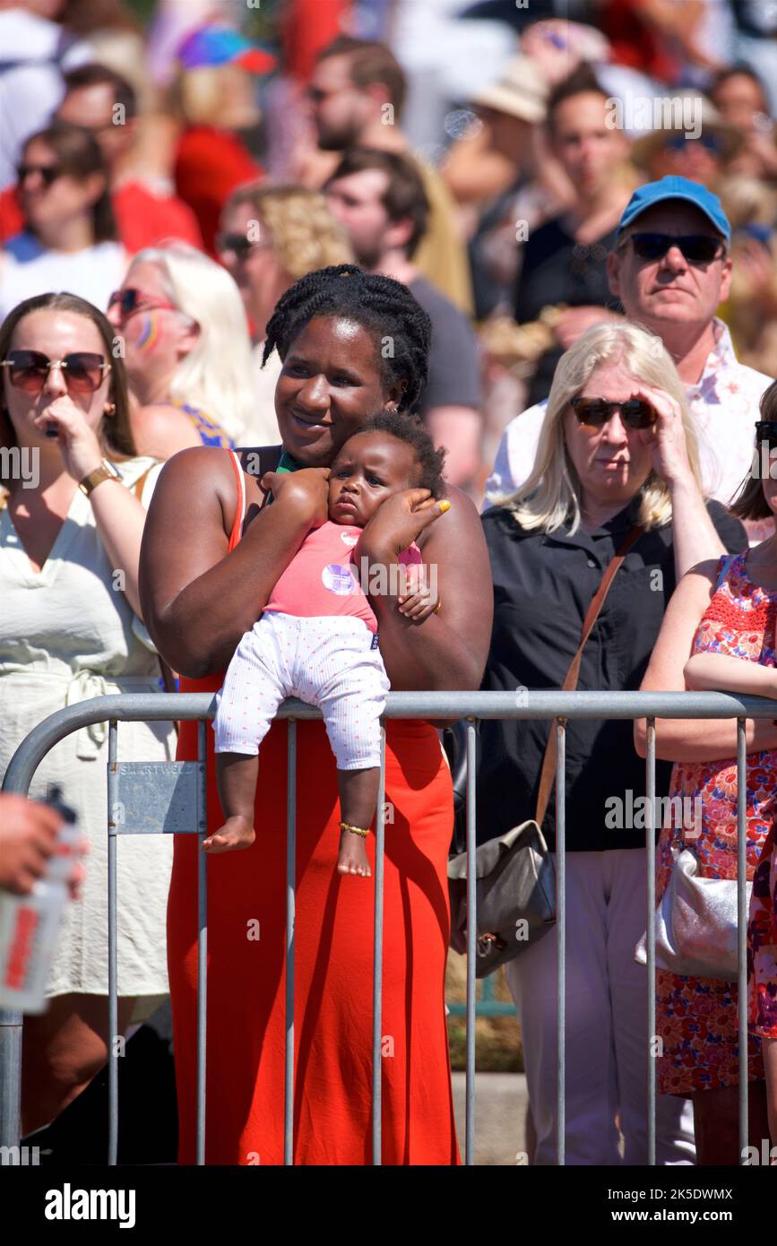 Brighton & Hove Pride Festival, Brighton & Hove, East Sussex, England. Mother holding baby whilst watching the parade from behind a metal barrier. Stock Photo