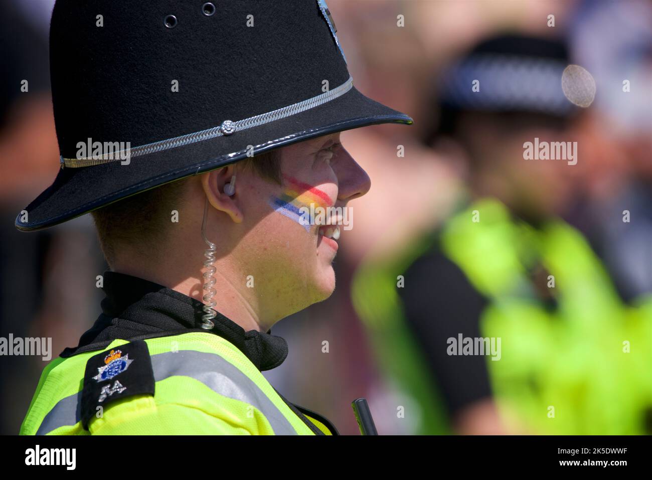 Brighton & Hove Pride Festival, Brighton & Hove, East Sussex, England. British policeman in uniform with rainbow flag painted on face. Stock Photo
