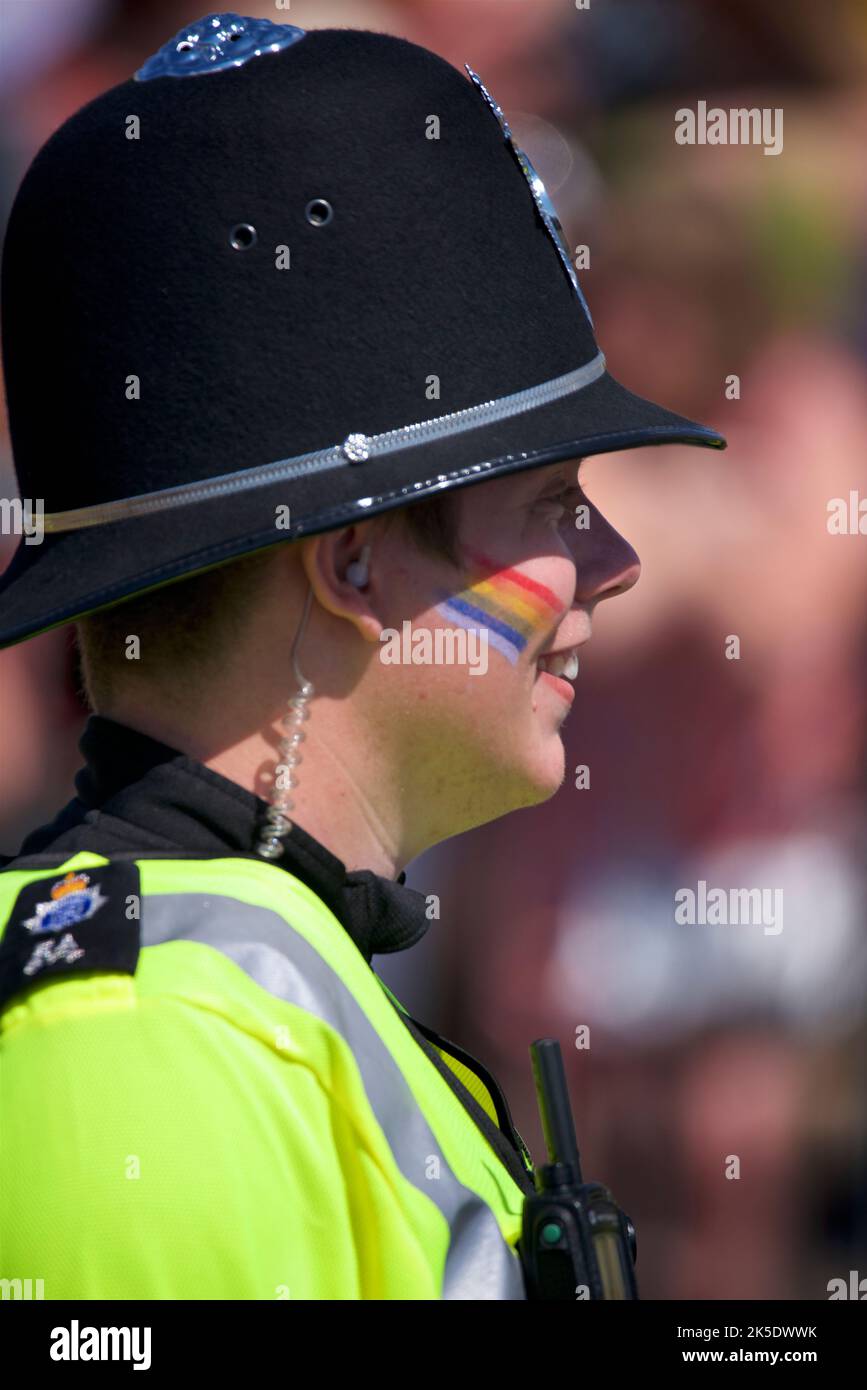 Brighton & Hove Pride Festival, Brighton & Hove, East Sussex, England. British policeman in uniform with rainbow flag painted on face. Stock Photo