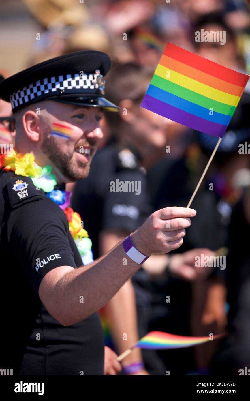 Brighton & Hove Pride Festival, Brighton & Hove, East Sussex, England. British policeman in uniform with rainbow flag painted on face and being waved in hand Stock Photo