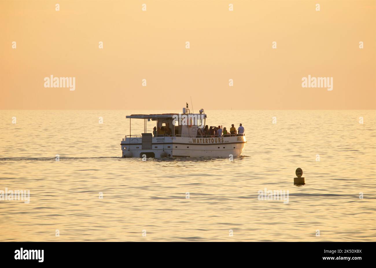 The Watertours boat from Brighton Marina cruising along the coast off Brighton and Hove at sunset in the fading golden light of a summer's day. Brighton & Hove, East Sussex, England, UK Stock Photo