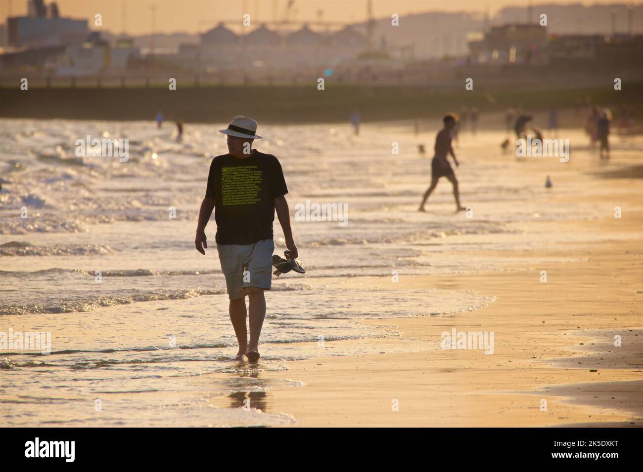 People on the beach at low tide in the late afternoon, July, Brighton & Hove, East Sussex, England, UK. Man in a panama hat walking along the shore. Stock Photo