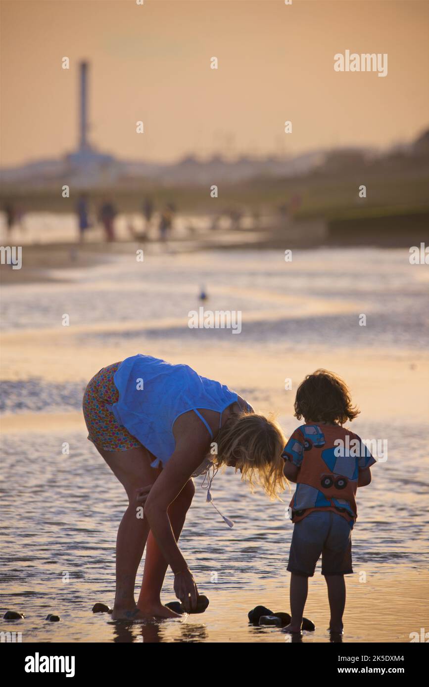 Mother and toddler on the beach in the late afternoon, July, Brighton & Hove, East Sussex, England, UK. In the shallow puddles on the sand at low tide. Stock Photo