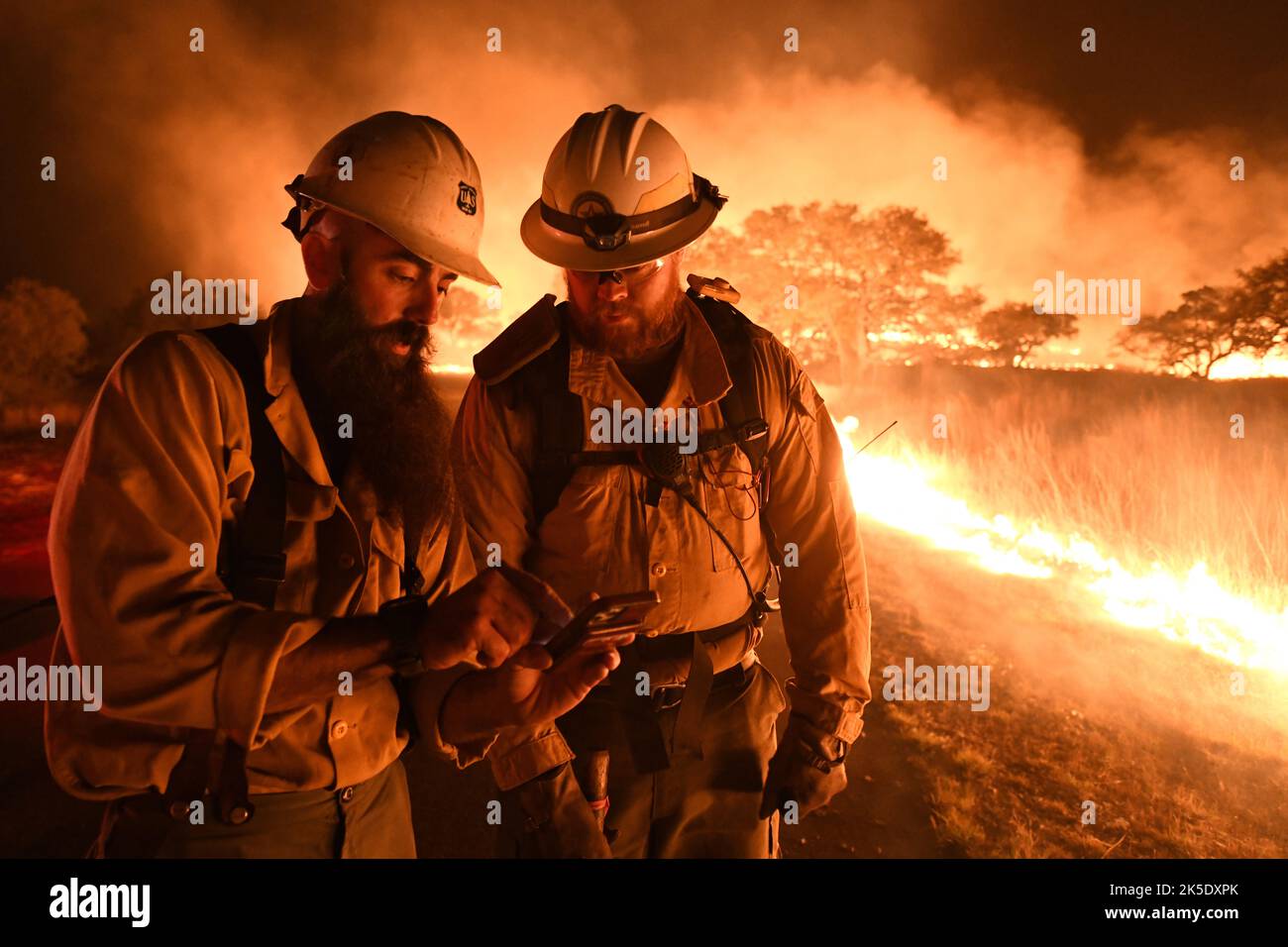 Texas State Forrest Service, Fredricksburg Task Force strike team firefighters (Dustin, left, and Cody, right) discuss a map to manage a large wildfire 9 April 2022 at Joint Base San Antonio - Camp Bullis demolition range area. JBSA-Camp Bullis comprises more than 27,000 acres of ranges, training areas, and wild-lands on San Antonio's North side and is a crucial training location for service members from Joint Base San Antonio.  An optimised / enhanced version of a USAF photo. Credit: USAF/B.Boisvert Stock Photo
