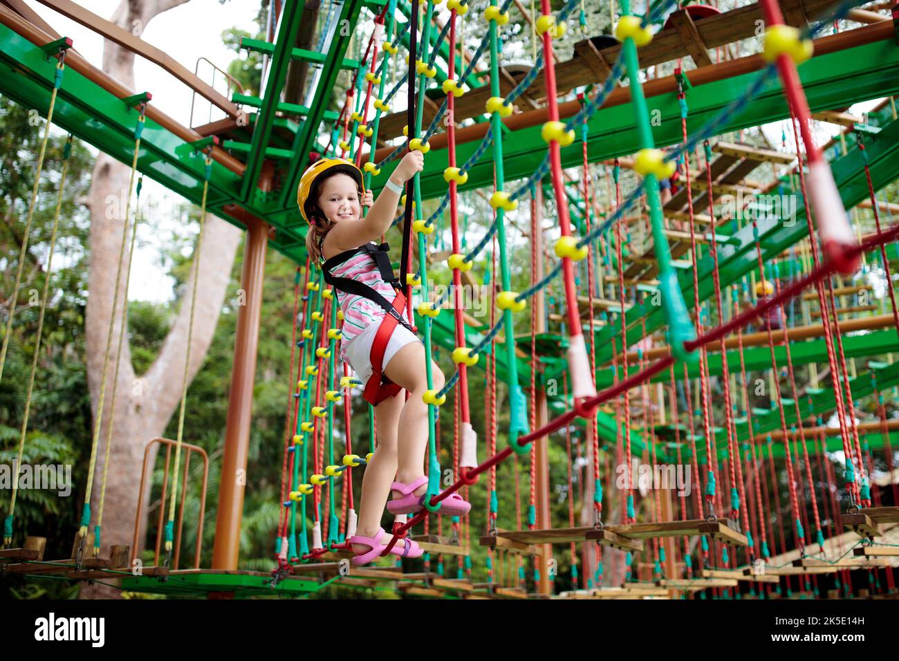 Child in forest adventure park. Kids climb on high rope trail. Agility
