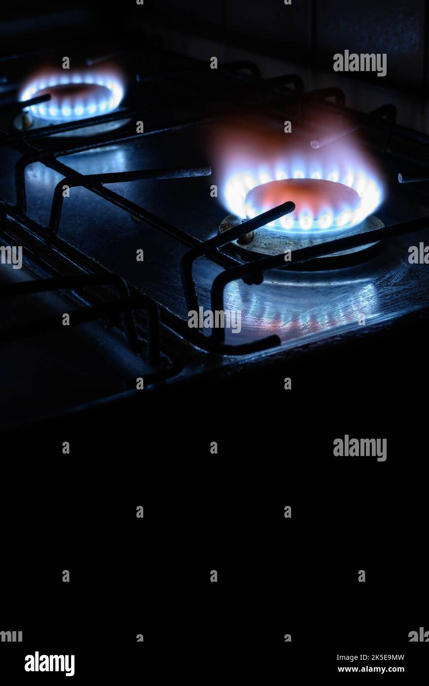 Gas stove at home, natural propane gas burns on dark background with black copy space, vertical view of blue fire flame of burners. Concept of gas cos Stock Photo