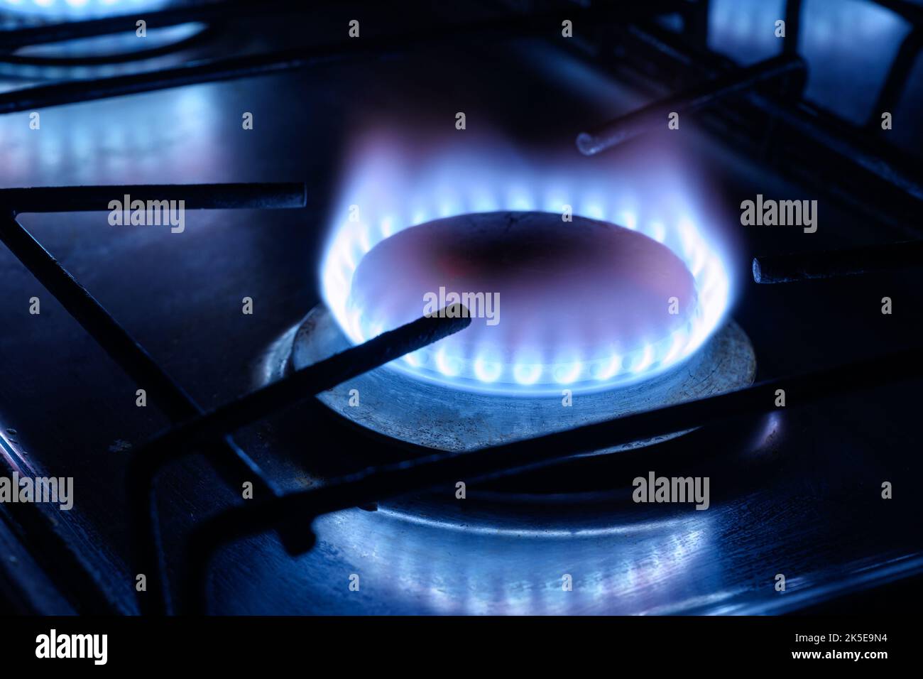 Gas burns in dark at home, blue fire flame of stove ring burners. Concept of natural pipeline gas cost and payment, energy crisis in Europe, supply in Stock Photo