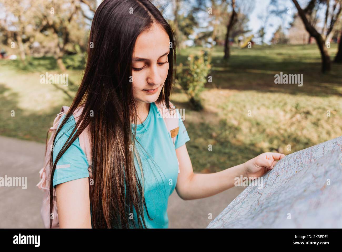 Young girl tourist, wearing turquoise t shirt and a pink backpack, checking the map during trek in the park Stock Photo