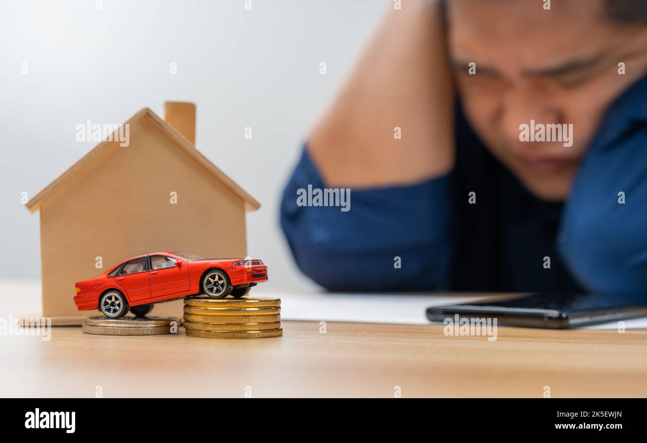 Unhappy Asian man holding a banknote and Making an account of income and expenses to pay the home loan and car loan, Concept loan payment and home ins Stock Photo
