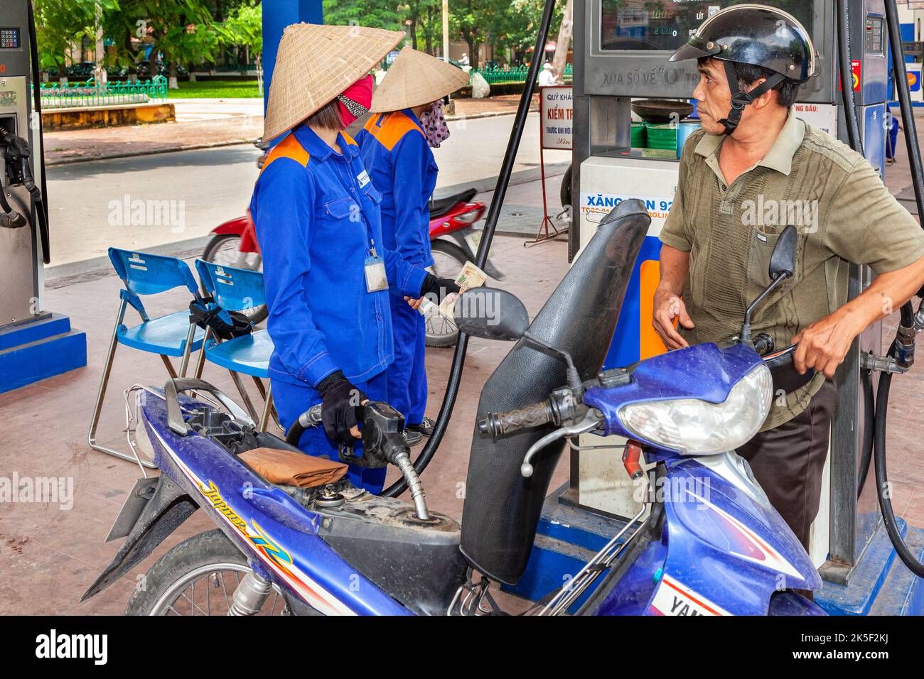Petrol filling station attendant wearing uniform and bamboo hat filling up motorcycle, Hai Phong, Vietnam Stock Photo
