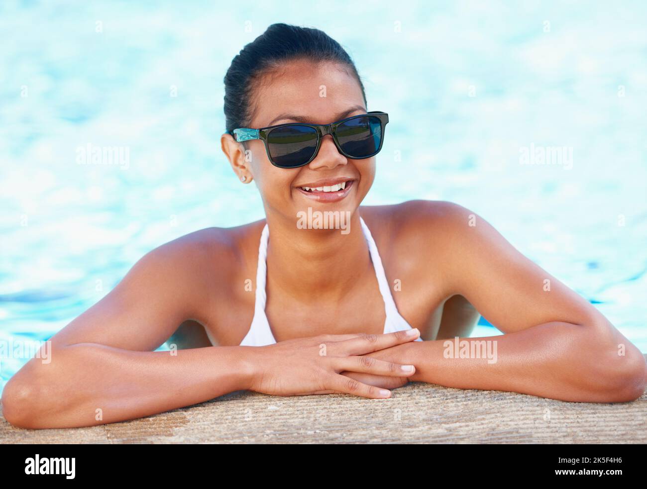 Looking good this summer. Cropped view of a young woman in a swimming pool smiling while wearing shades. Stock Photo