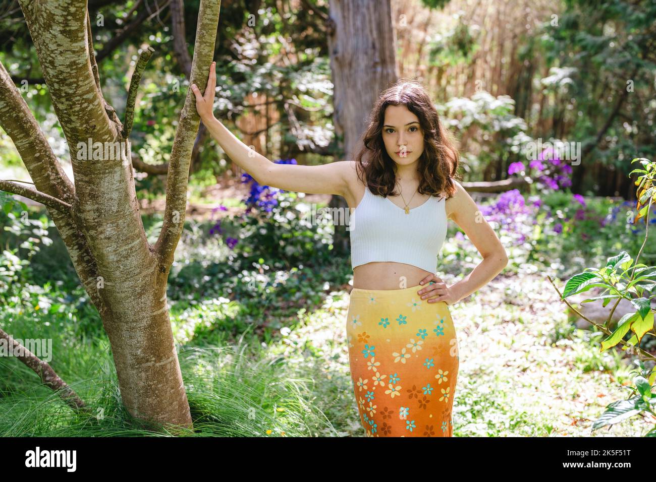 Portrait of a Young Woman in Colorful Orange Floral Print Skirt Standing Surrounded by Flowers in a Botanical Garden Stock Photo