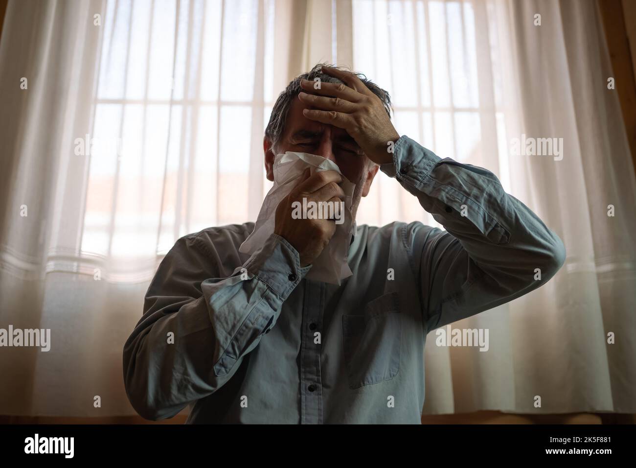 Sick man with cold, blowing his nose and with headache and fever Stock