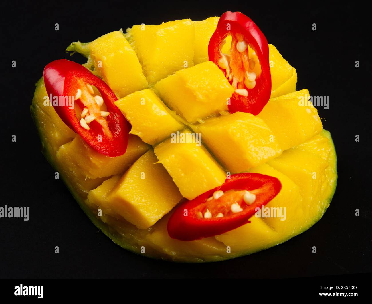 Close-up of diced half of mango and sliced red hot pepper on solid black background. Ingredients for salad. Stock Photo