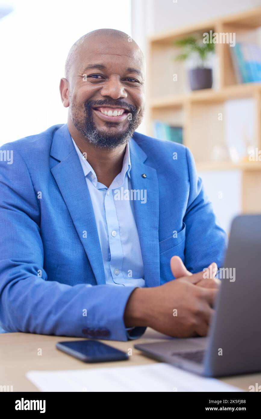 Happy, smile and portrait of an African businessman sitting at his desk and working on a laptop in his office. Happiness, leader and black man leader Stock Photo