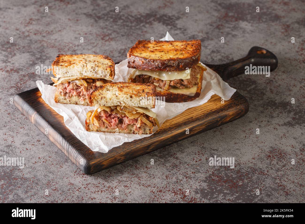 patty melt sandwich has a burger patty covered with melted Swiss cheese, caramelized onions, and griddled slices of rye bread closeup on the wooden bo Stock Photo