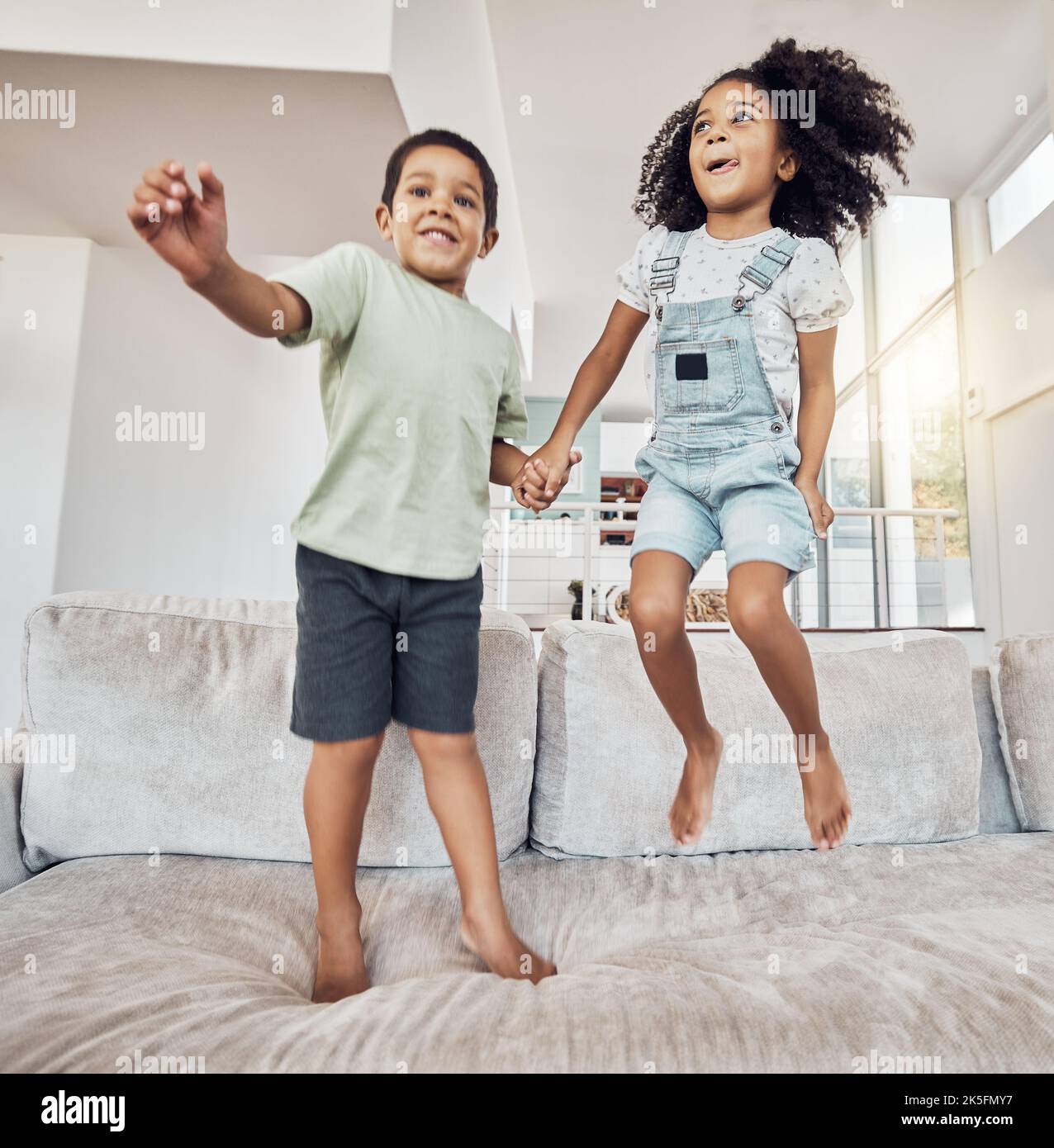 Children, brother and sister bonding and jumping on sofa in house, home or hotel living room in fun, play and energy game. Smile, happy or adhd kids Stock Photo