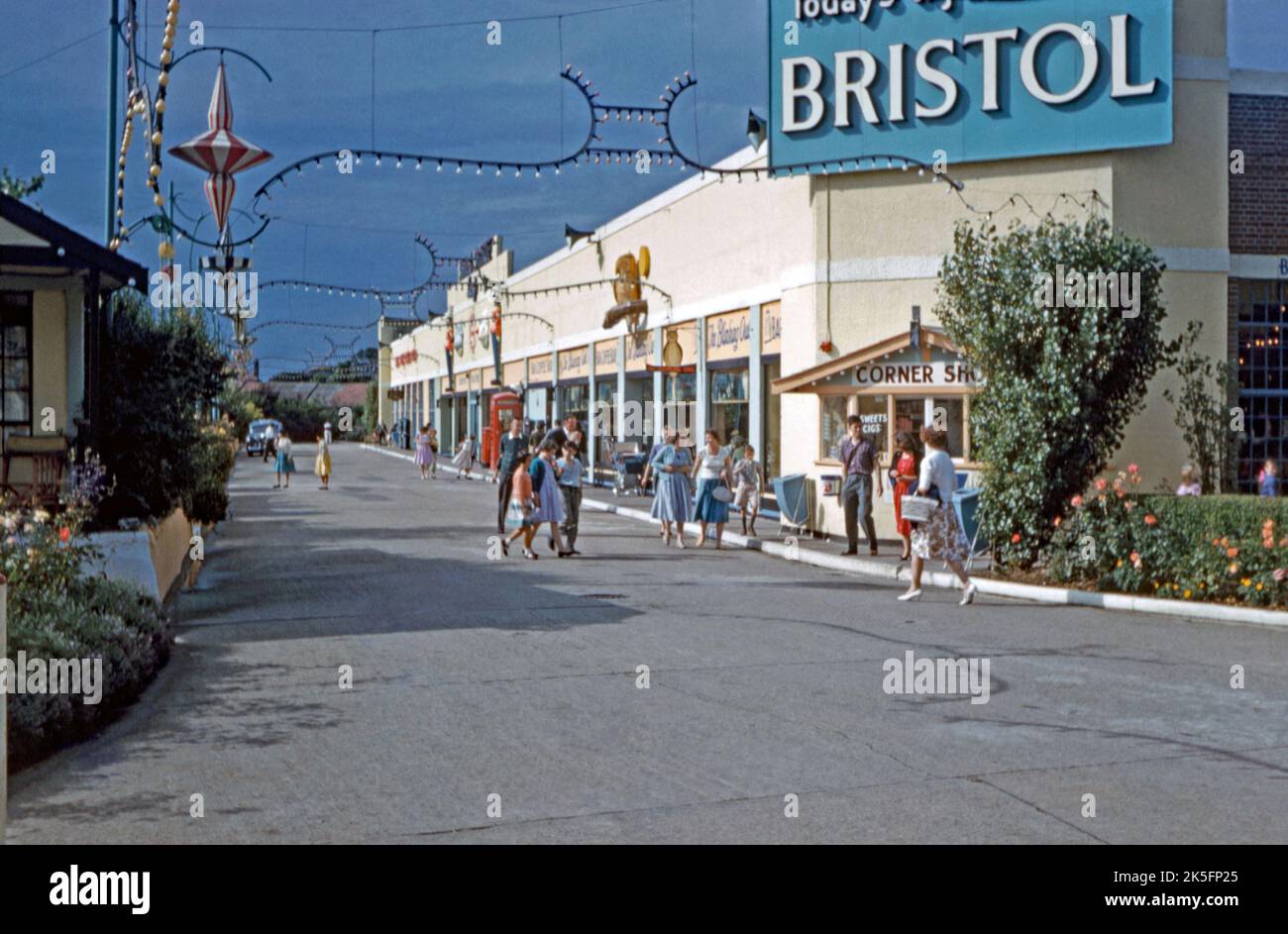 The shopping parade at Butlin’s Clacton holiday camp in the mid-1960s. The kiosk corner shop sells ‘sweets and cigs’. A sign for ‘The Blinking Owl’ is for an onsite pub. Billy Butlin created a new holiday camp at Clacton-on-Sea, Essex, England, UK, by buying and refurbishing the West Clacton Estate, an amusement park to the west of the town. The Clacton camp was open until 1983 when the holiday camp was closed and sold – it reopened it as a theme park called Atlas Park. Atlas Park only lasted a year and the land was then sold and redeveloped for housing – a vintage 1960s photograph. Stock Photo