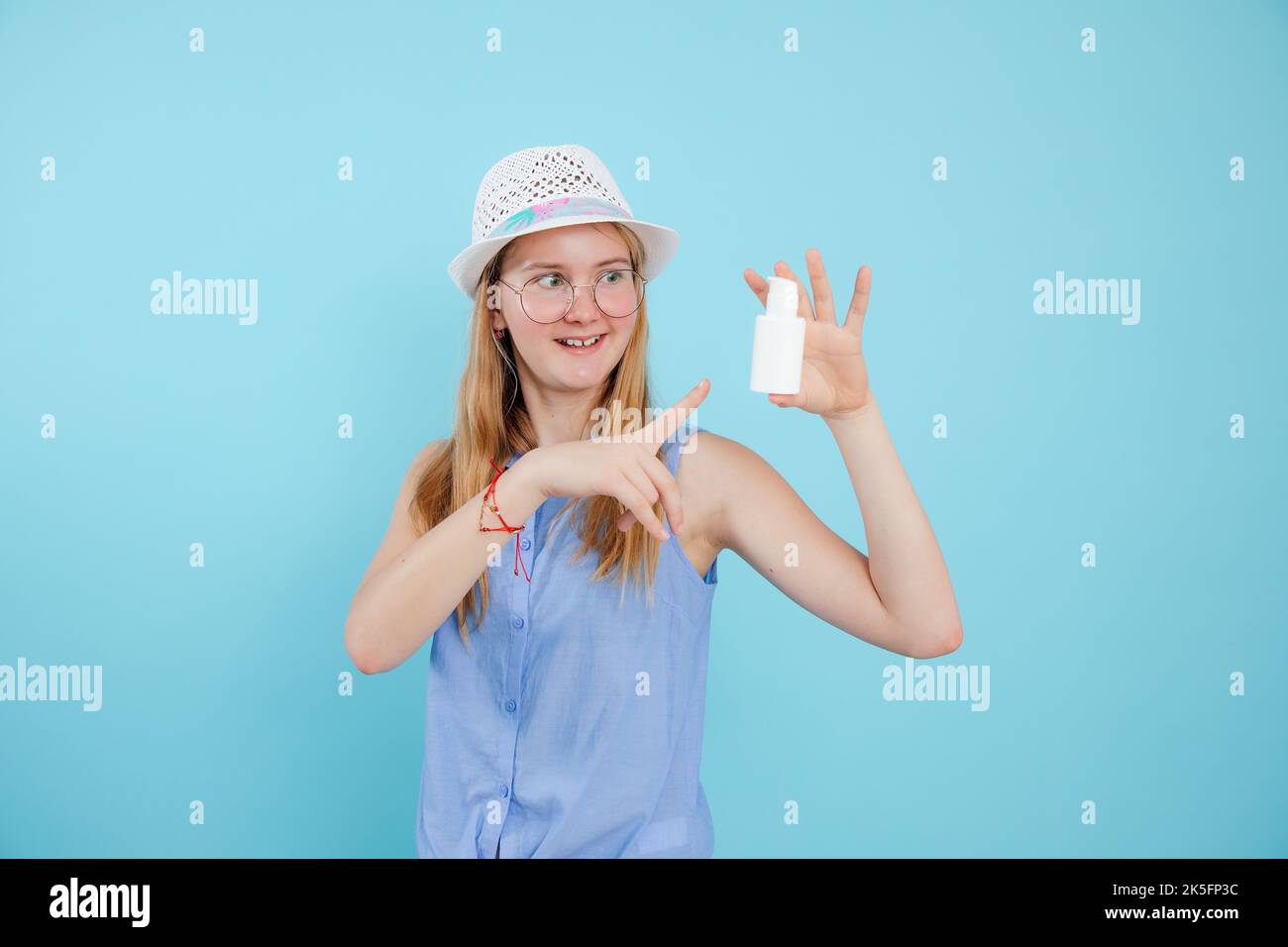 Pretty teenage girl advertise beauty remedy for acne on blue empty background, free copy space. Smiling young lady in glasses and summer panama point Stock Photo