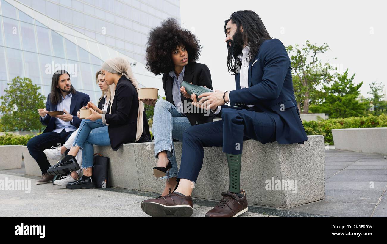 Business man with disability adjusting his prosthetic leg while teamwork having lunch break outside the office Stock Photo