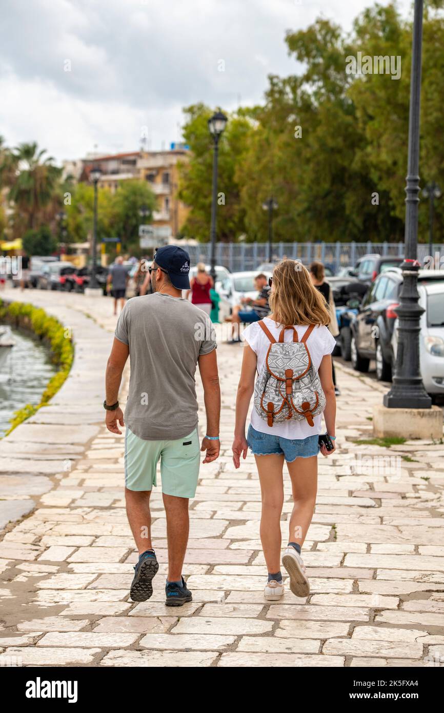 young couple man and woman walking along a sea wall at the seaside on the greek holiday island of zante or zakynthos in greece. Stock Photo