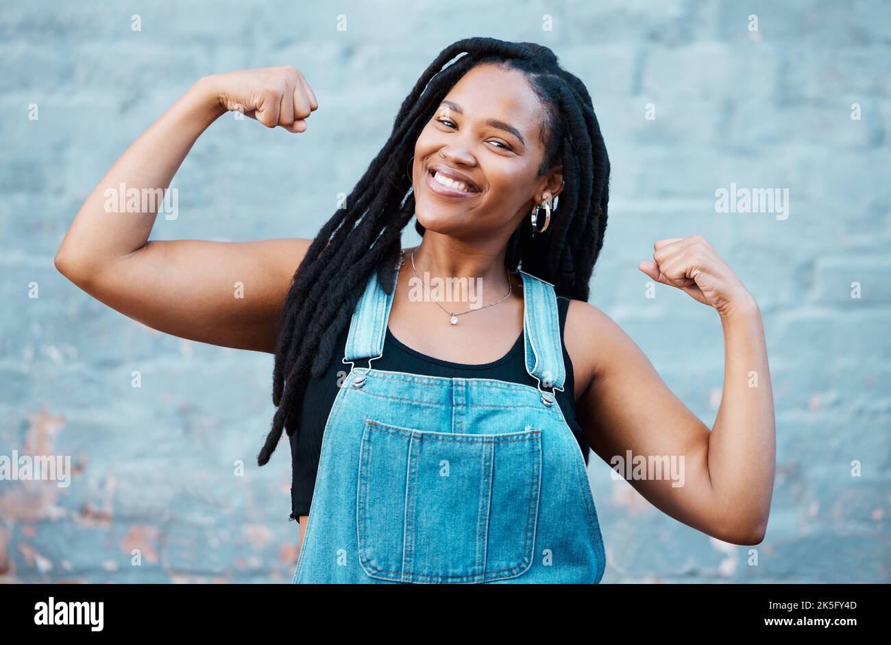 Happy black woman, portrait smile and muscle power, strength and confident pose on wall background. Proud African female flexing biceps, muscles and Stock Photo