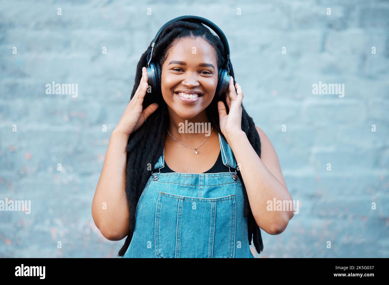 Gen z black woman, music headphones and portrait on wall background in Nigeria city listening to radio, audio and sound. Happy young african girl Stock Photo