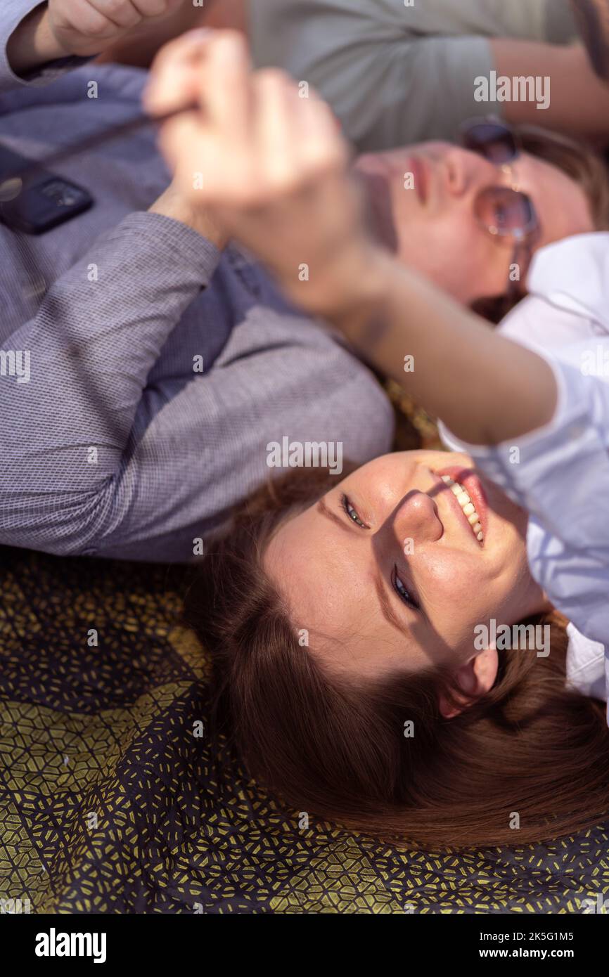 Portrait of young beautiful woman holding sunglasses. Couple relaxing while laying down on green blanket in the park Stock Photo
