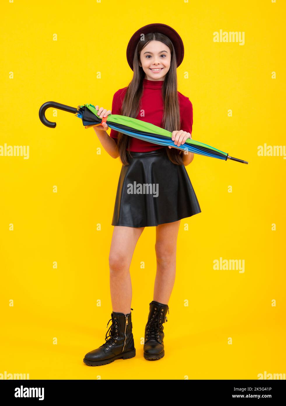 Autumn kids weather, full length. Child teenager girl with umbrella in autumn skirt, sweater, boots and hat isolated on yellow studio background Stock Photo