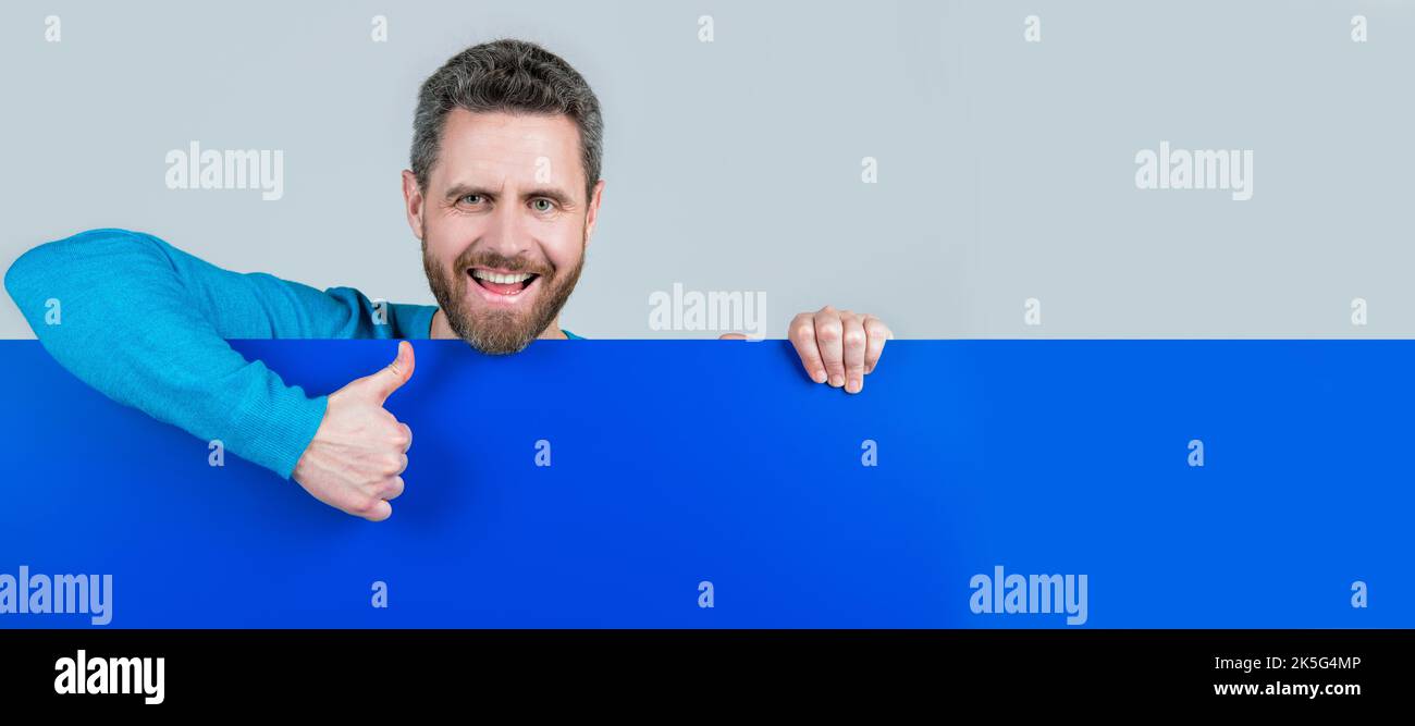 Man face portrait, banner with copy space. product presenting. presenting novelty information. male behind blue paper show thumb up. Stock Photo