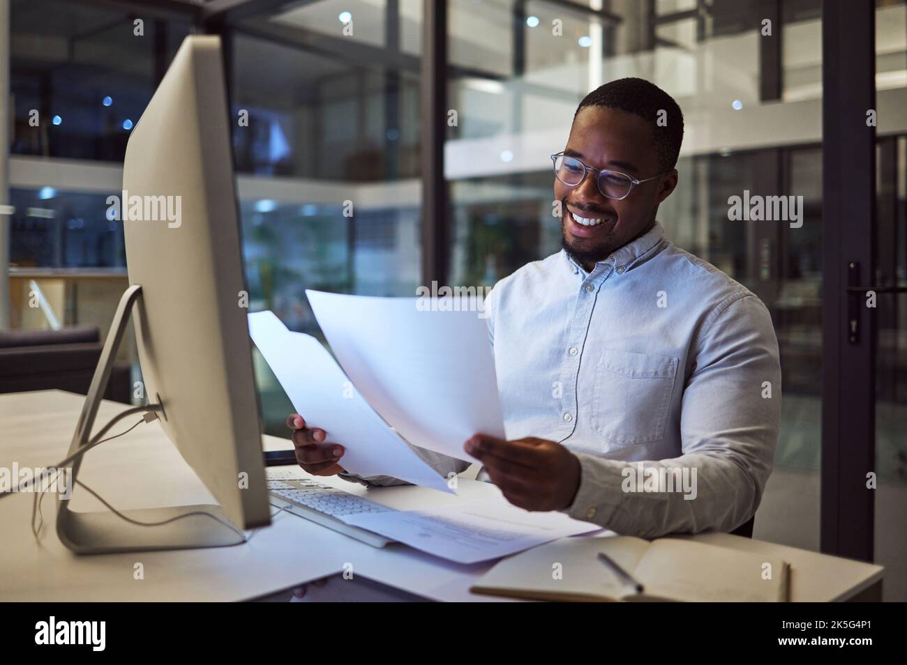 Documents, night and computer with a businessman working at his desk late in the office. Paperwork, finance and tax with a male employee at work for Stock Photo