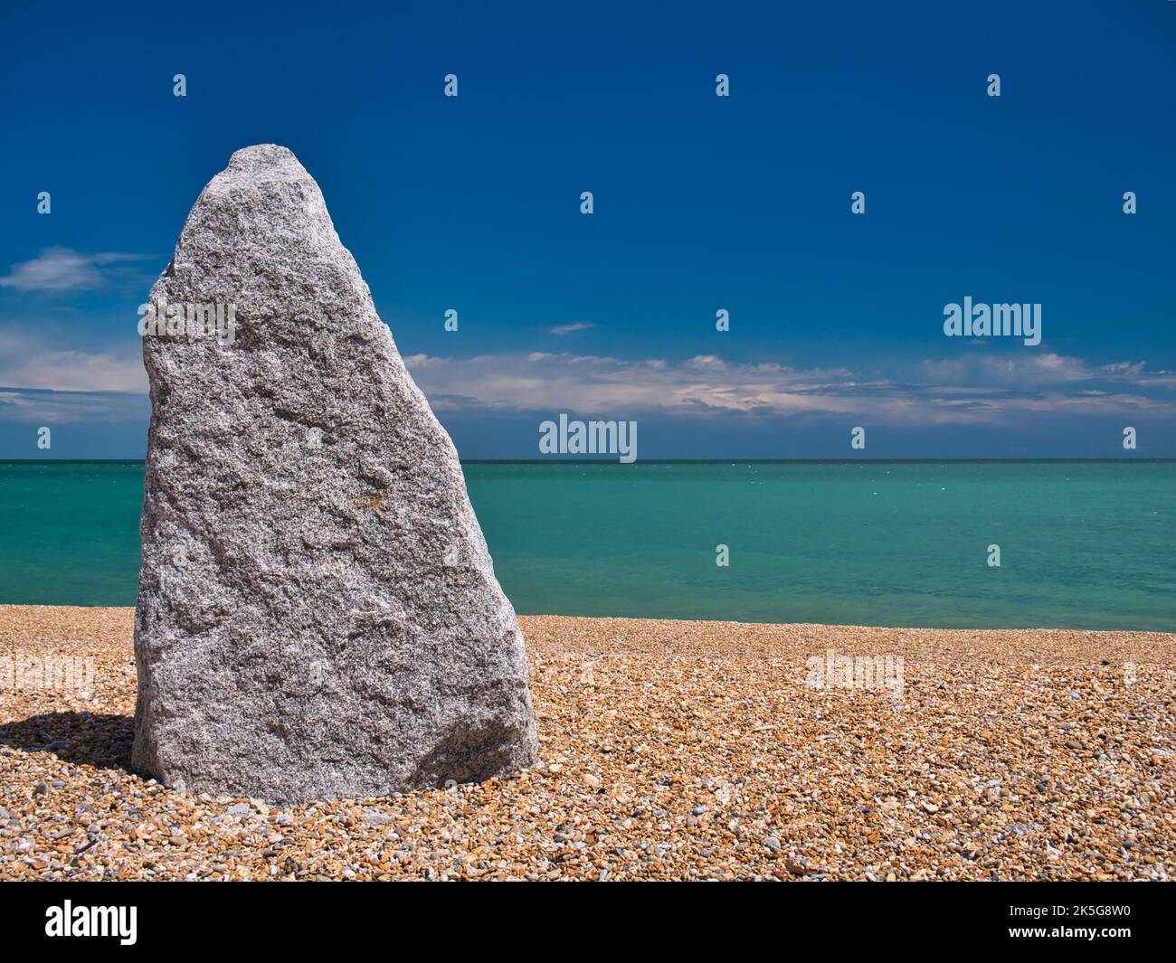 A tall, 2m, grey standing stone on the shingle beach at Walmer, Deal, Kent, UK. Taken on a sunny day with blue sky and a turquoise sea. Stock Photo