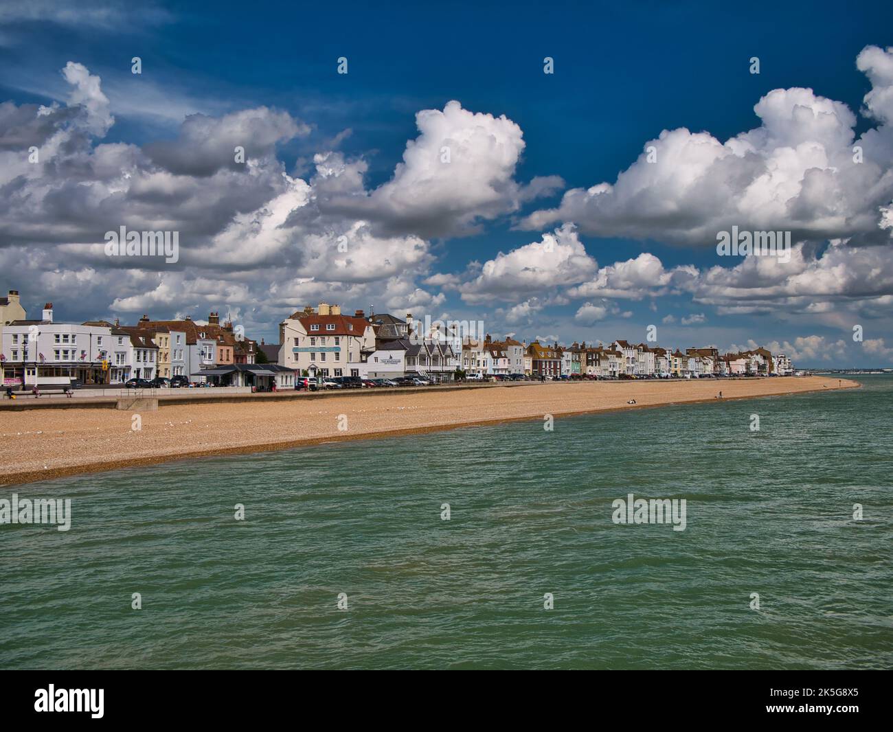 The pebble beach and seafront buildings at Deal, Kent, England, UK. Taken from the pier on a sunny day in summer with blue sky and white clouds. Stock Photo