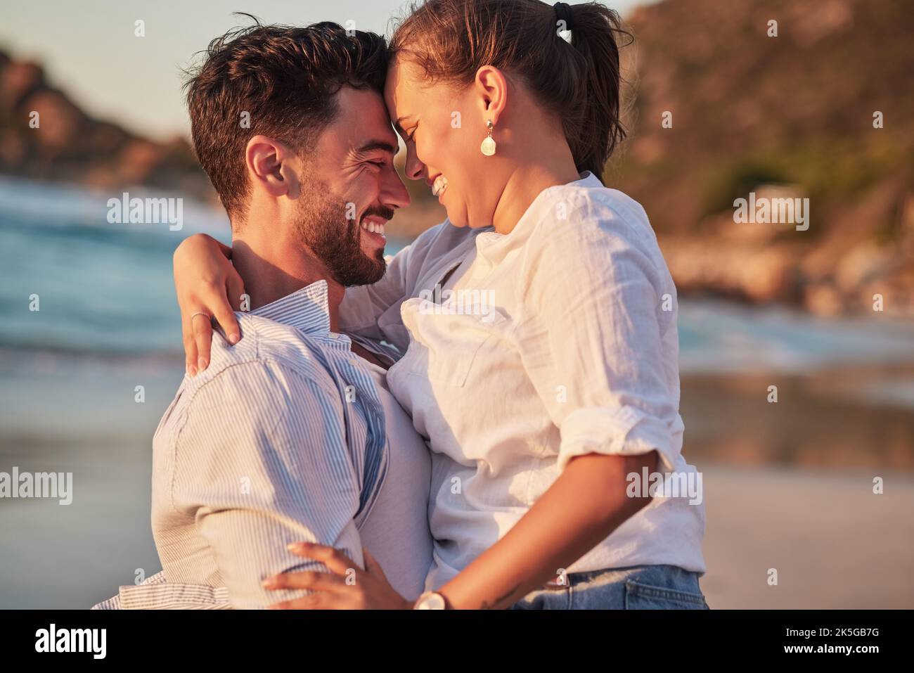 Couple, laughing or love hug on beach at sunset for anniversary event, honeymoon celebration or engagement. Smile, happy or comic man and woman Stock Photo