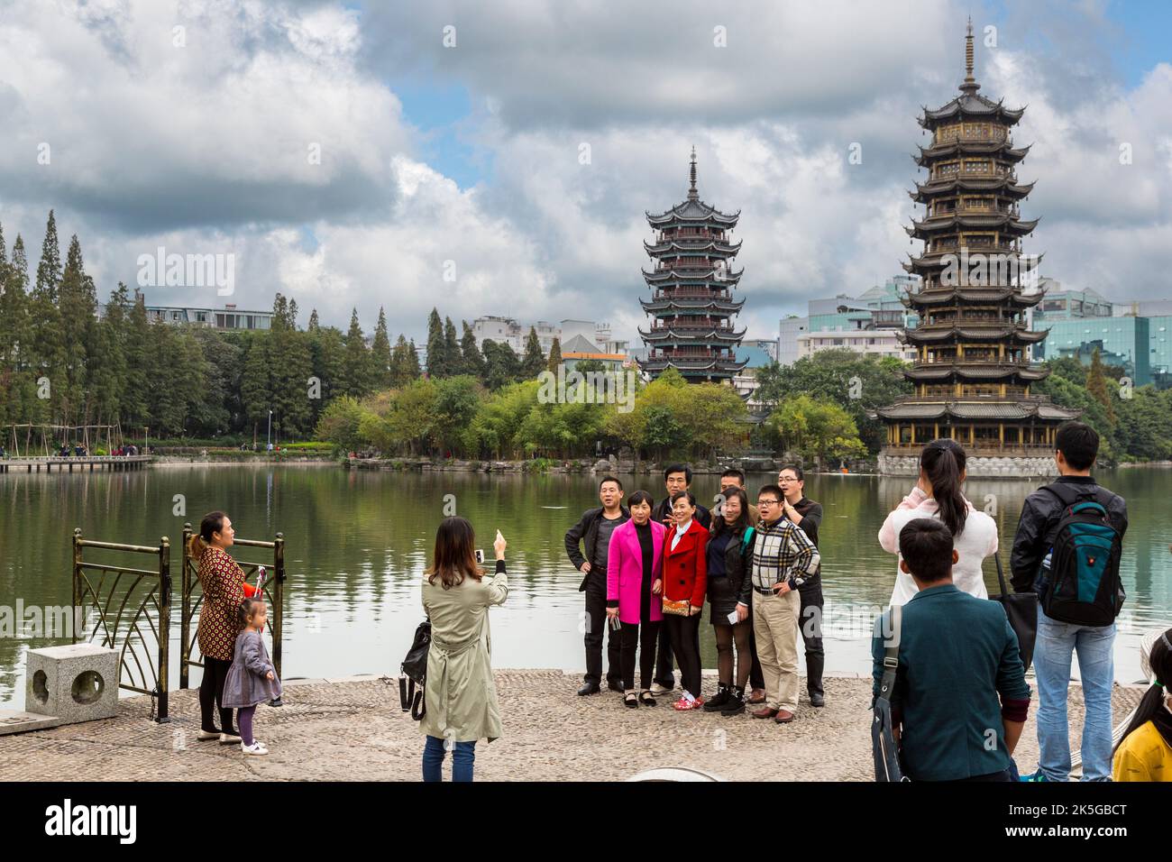 Guilin, China.  Visitors Taking Pictures in Gardens along Shan (Fir) Lake.  Sun and Moon Pagodas in Background. Stock Photo
