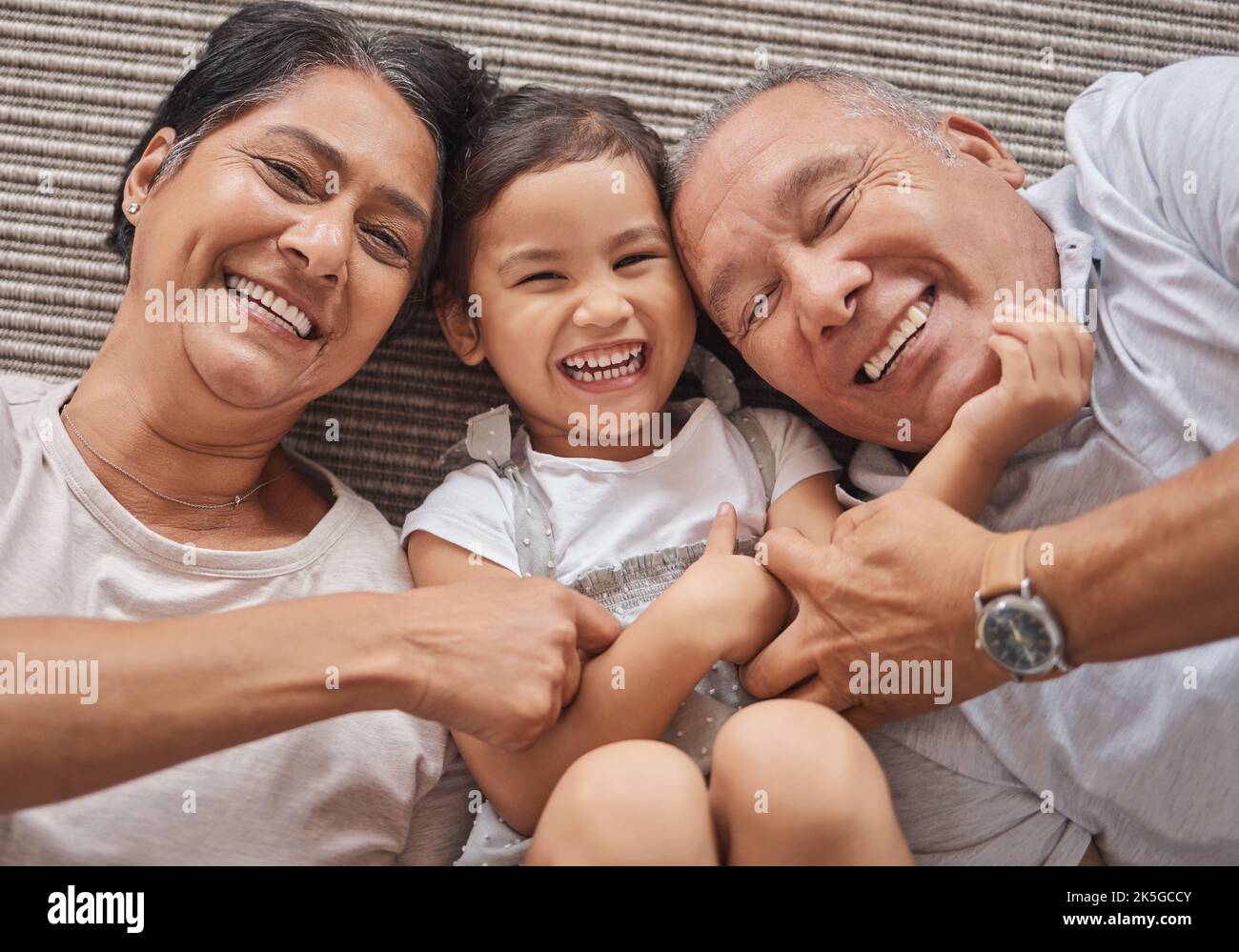 Kid, grandma and grandpa lying on floor playing at home, spending family time together above view. Happy grandparents bonding with little girl in Stock Photo