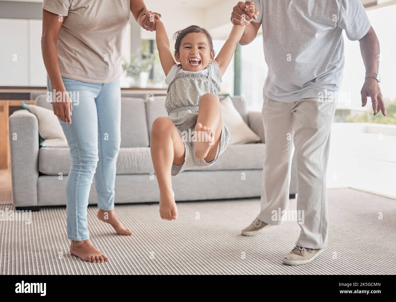 Family, child holding hands and swinging in fun living room play time, childhood and bonding at home. Happy kid smile in playful childcare and joyful Stock Photo