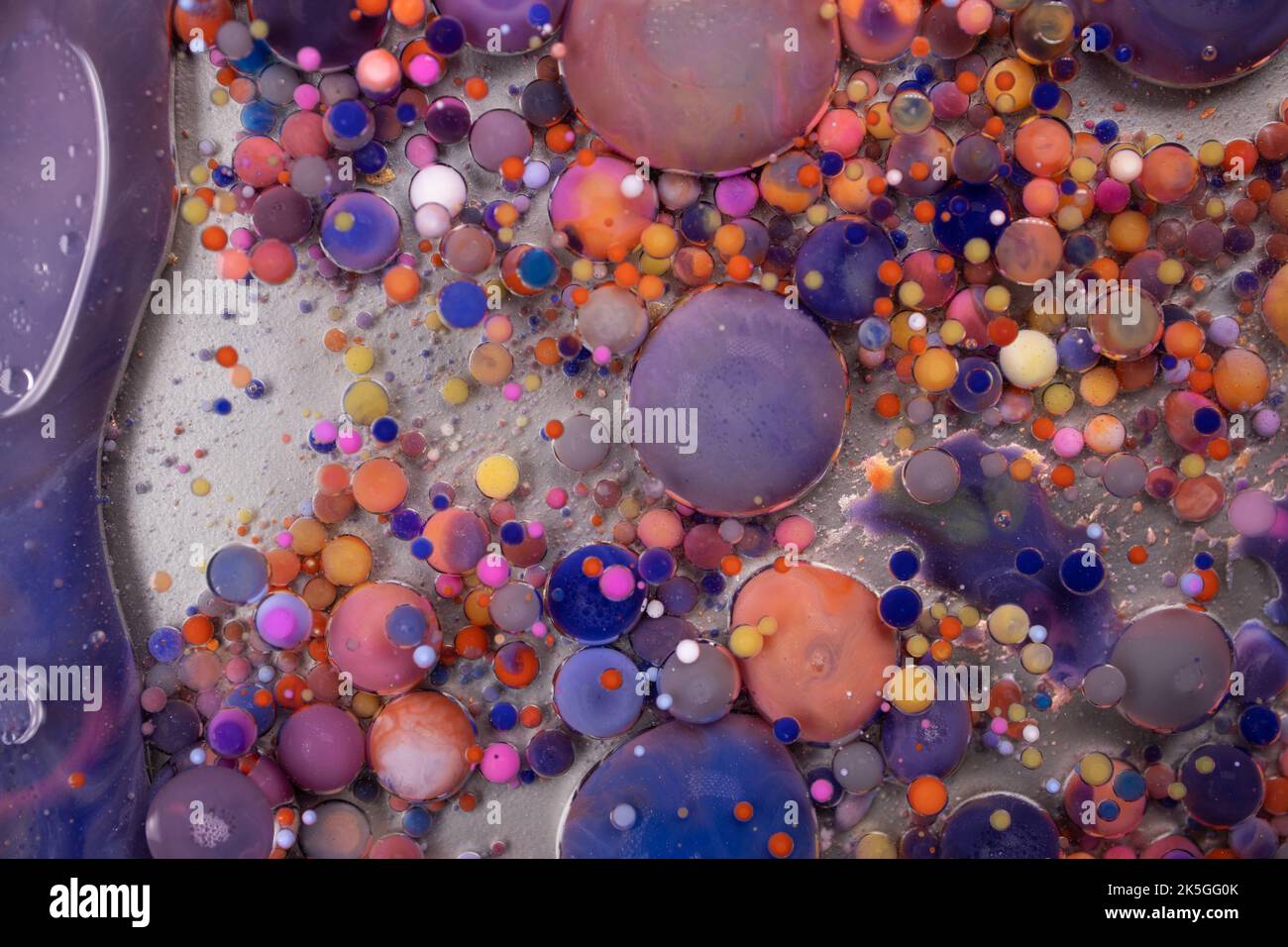 Acrylic paint balls abstract texture. Bright colors fluid, flowing wallpaper design. Purple, blue, pink and yellow liquids mix. Stock Photo